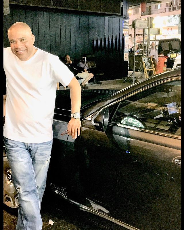 Kerry Gordy in a white t-shirt and blue jeans posing in front of his car.